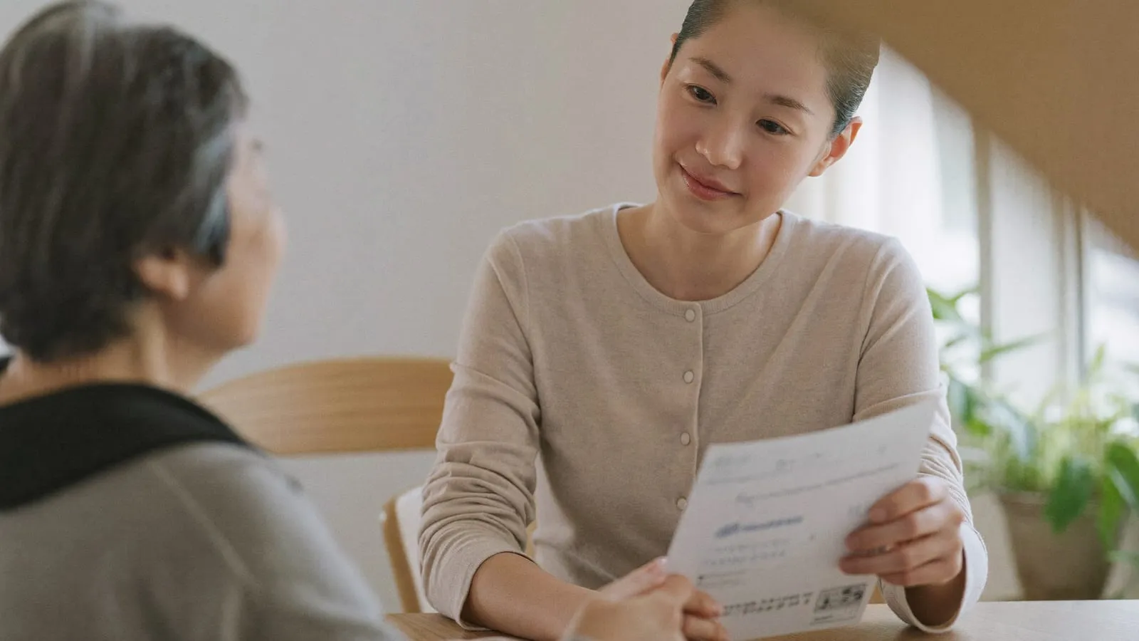 資料を手に、高齢の女性へ穏やかに説明する相談員のイメージ